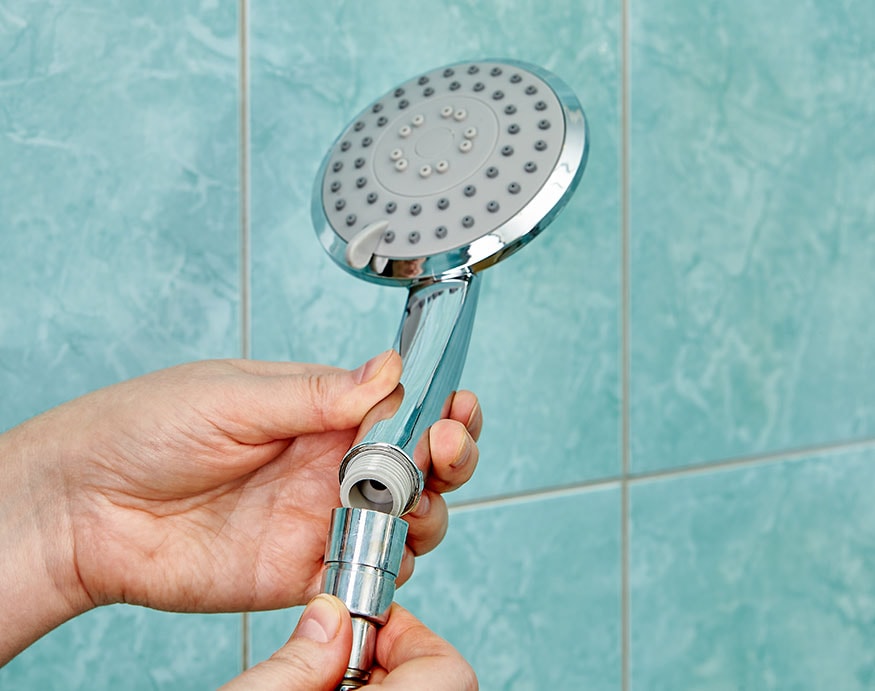 A hand removing an old shower head from hose
