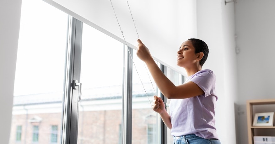 a woman closing the window roller blinds